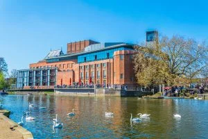 a multi story, brick and glass contemporary office building on the river with swans in the foreground